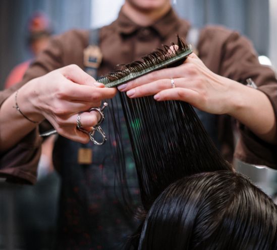 A hairstylist pulls a person's hair straight and begins to clip it with scissors.